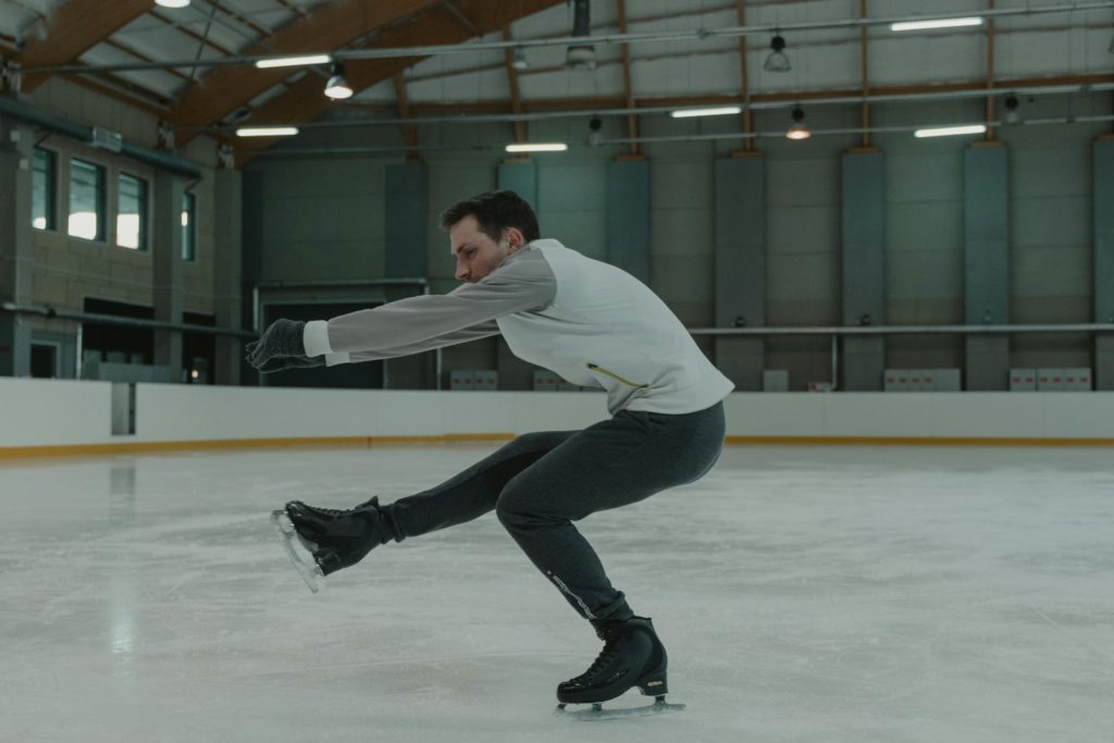 Man executing a figure skating maneuver on an indoor rink, showcasing skill and balance.